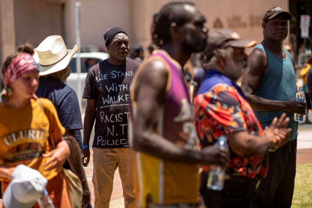 A crowd of Indigenous people in Australia stands together looking anxious and worried. 0............................................................/;;;;;',llllllllllllllllllllll