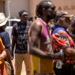 A crowd of Indigenous people in Australia stands together looking anxious and worried. 0............................................................/;;;;;',llllllllllllllllllllll