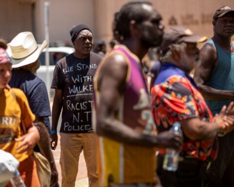 A crowd of Indigenous people in Australia stands together looking anxious and worried. 0............................................................/;;;;;',llllllllllllllllllllll