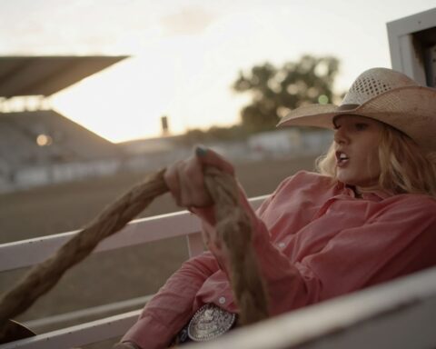 A cowgirl wearing a pink collared shirt and white cowboy hat sits atop a horse.