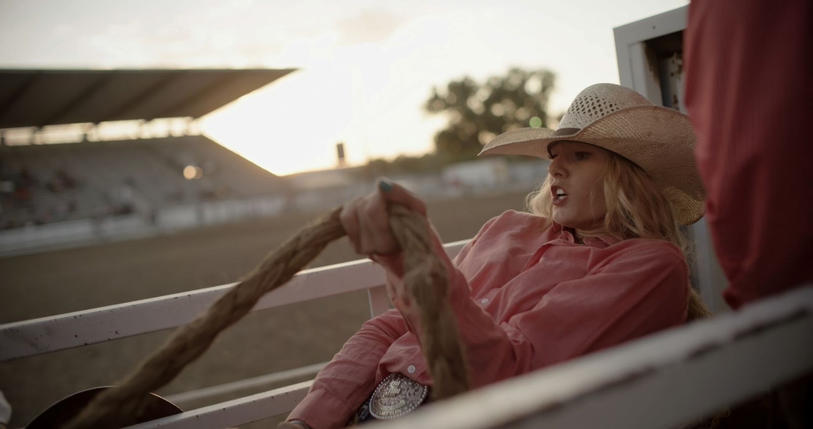 A cowgirl wearing a pink collared shirt and white cowboy hat sits atop a horse.