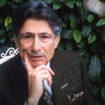 Academic Edward Said looks directly into the camera, posing with this chin on his hand to express thought. He is wearing a suit and there are green leaves behind him. The portrait is bordered by strips of black and white photographs.
