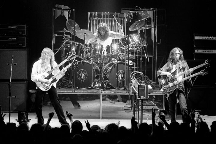A black and white photo shows the rock band Rush performing on stage.