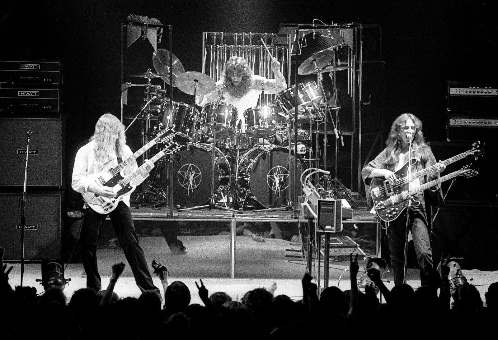 A black and white photo shows the rock band Rush performing on stage.