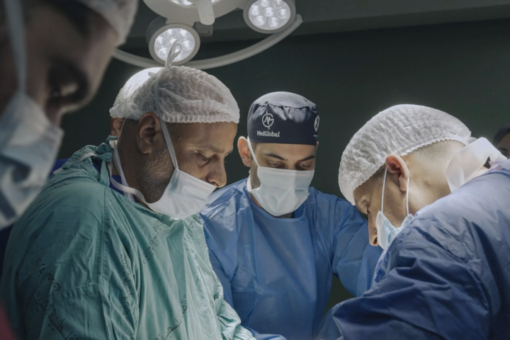 A team of doctors performs a surgery around an operating table.
