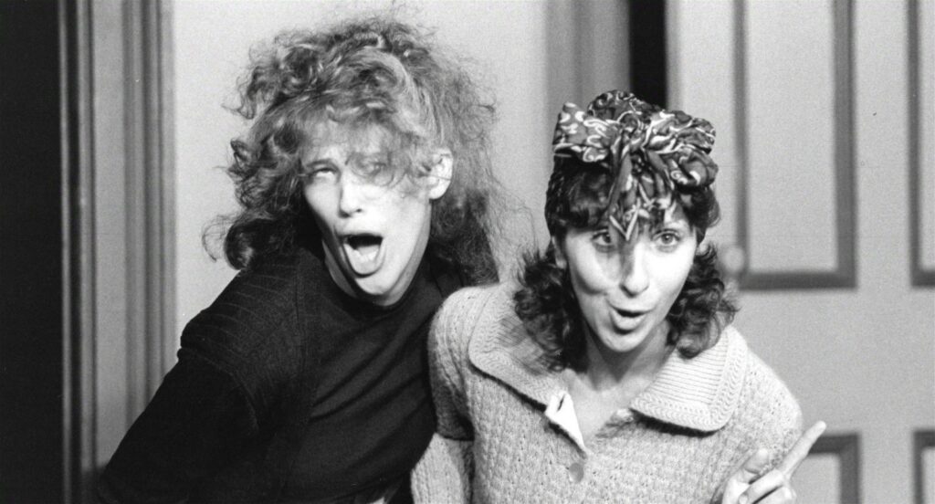 A black and white photo shows young comedians Catherine O'Hara and Andrea Martin making funny faces and being goody during a sketch for SCTV.