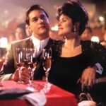A film still from Goodfellas (1990) depicts actors Ray Liotta and Lorraine Bracco seated at a table in a nightclub.