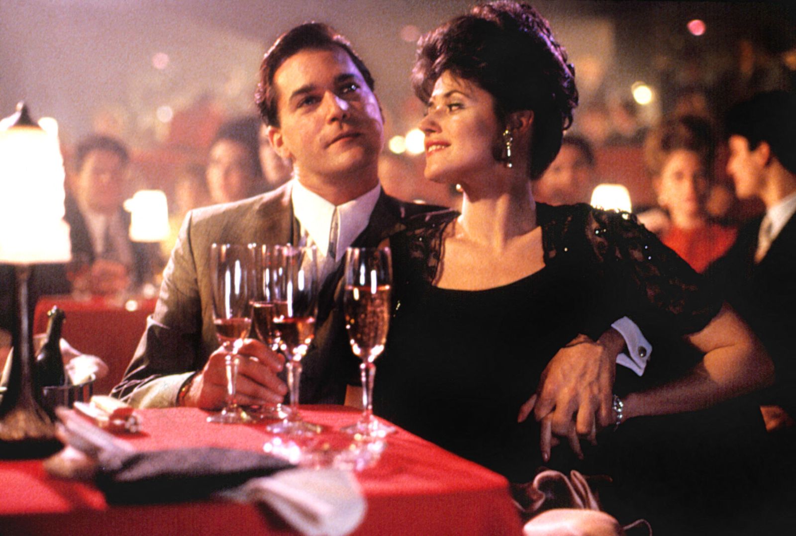 A film still from Goodfellas (1990) depicts actors Ray Liotta and Lorraine Bracco seated at a table in a nightclub.