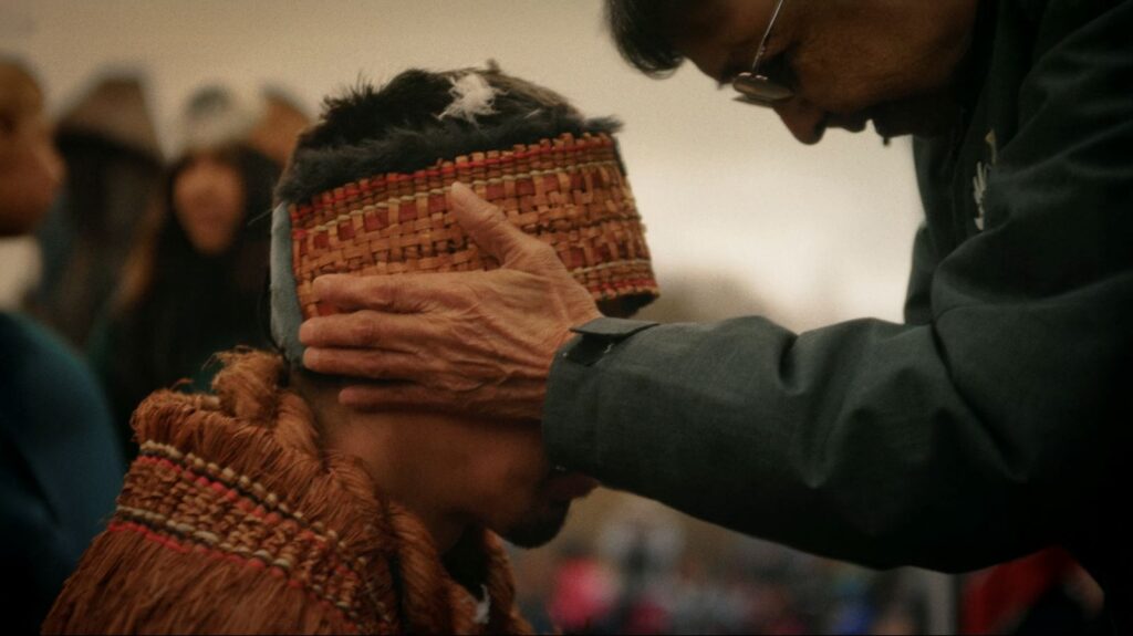 An Elder places his hand on a man in regalia during the sputc ceremony, a moment of blessing.