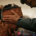 An Elder places his hand on a man in regalia during the sputc ceremony, a moment of blessing.