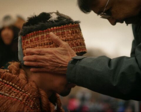 An Elder places his hand on a man in regalia during the sputc ceremony, a moment of blessing.